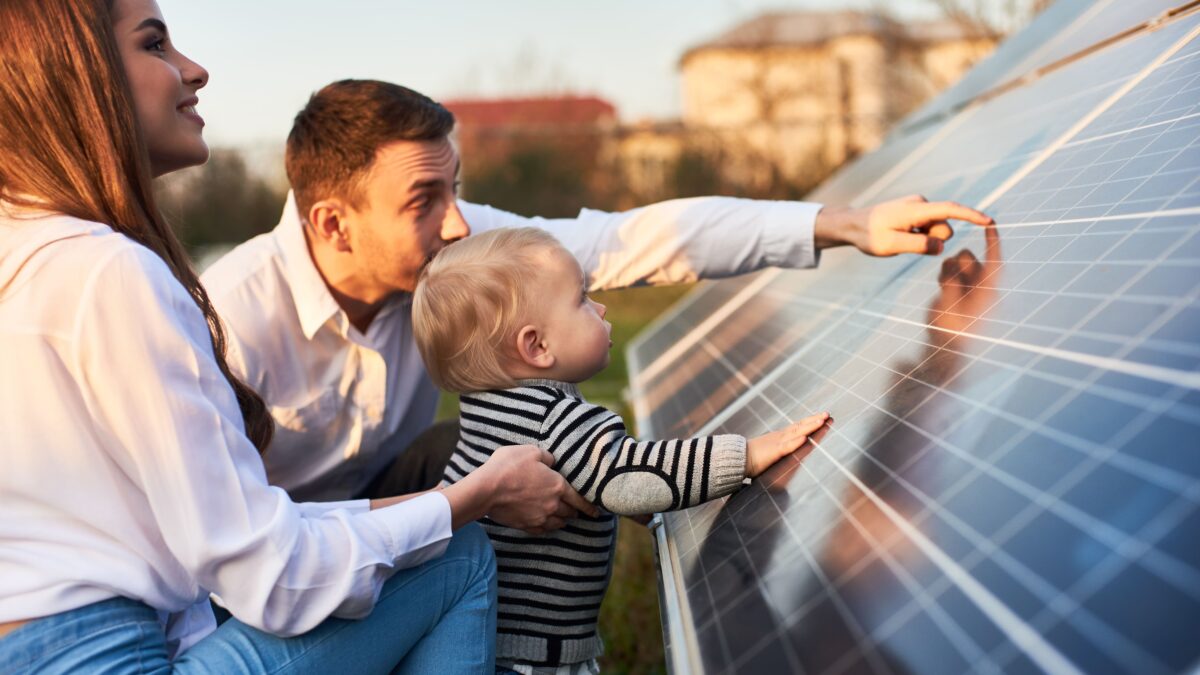 Side close-up shot of a young modern family with a little son getting acquainted with solar panel on a sunny day