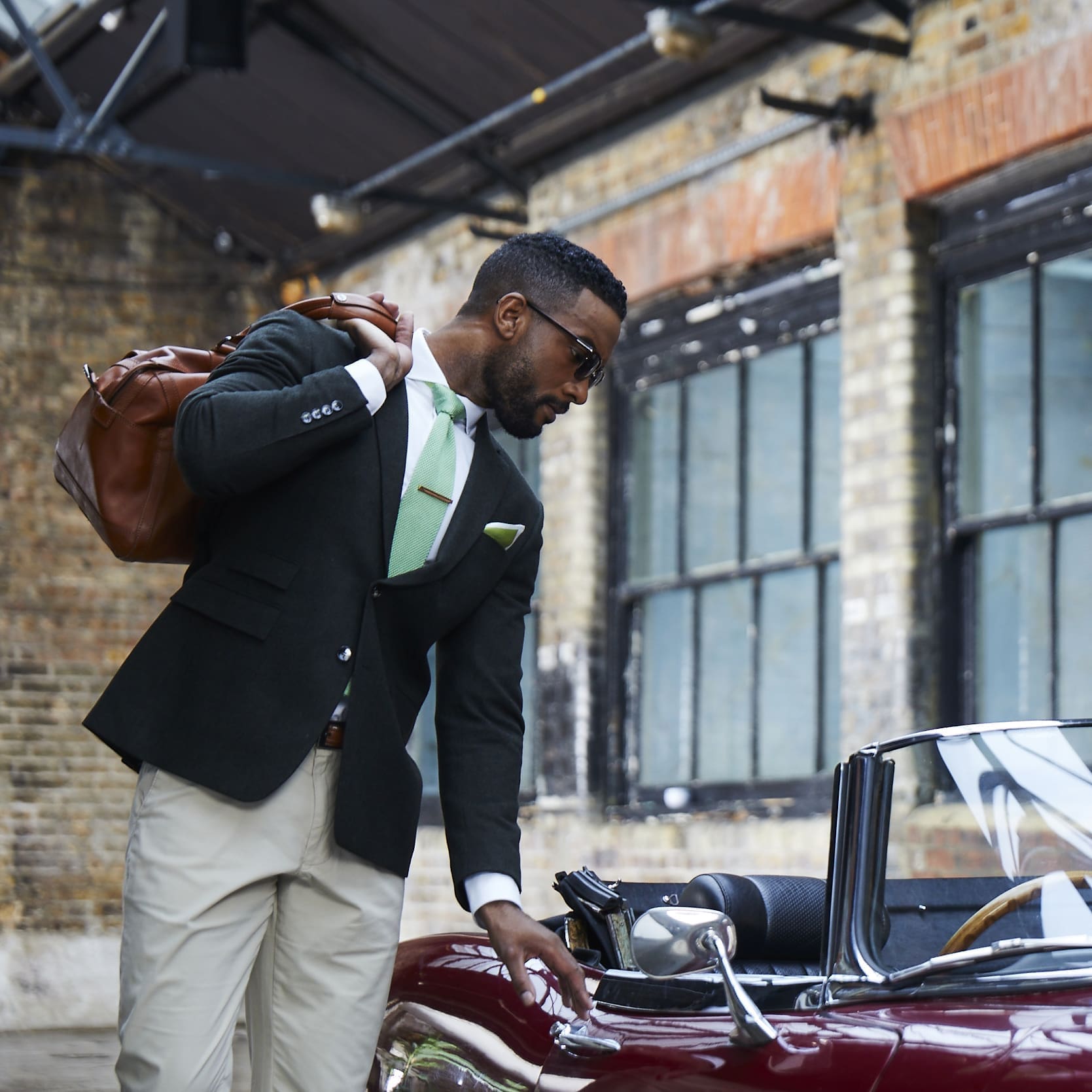 Stylish black man in suit with leather bag getting into a red convertible classic car
