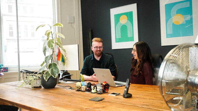 Developer, Matt, and Account Manager, Sarinda, chatting at Matt's desk in the studio